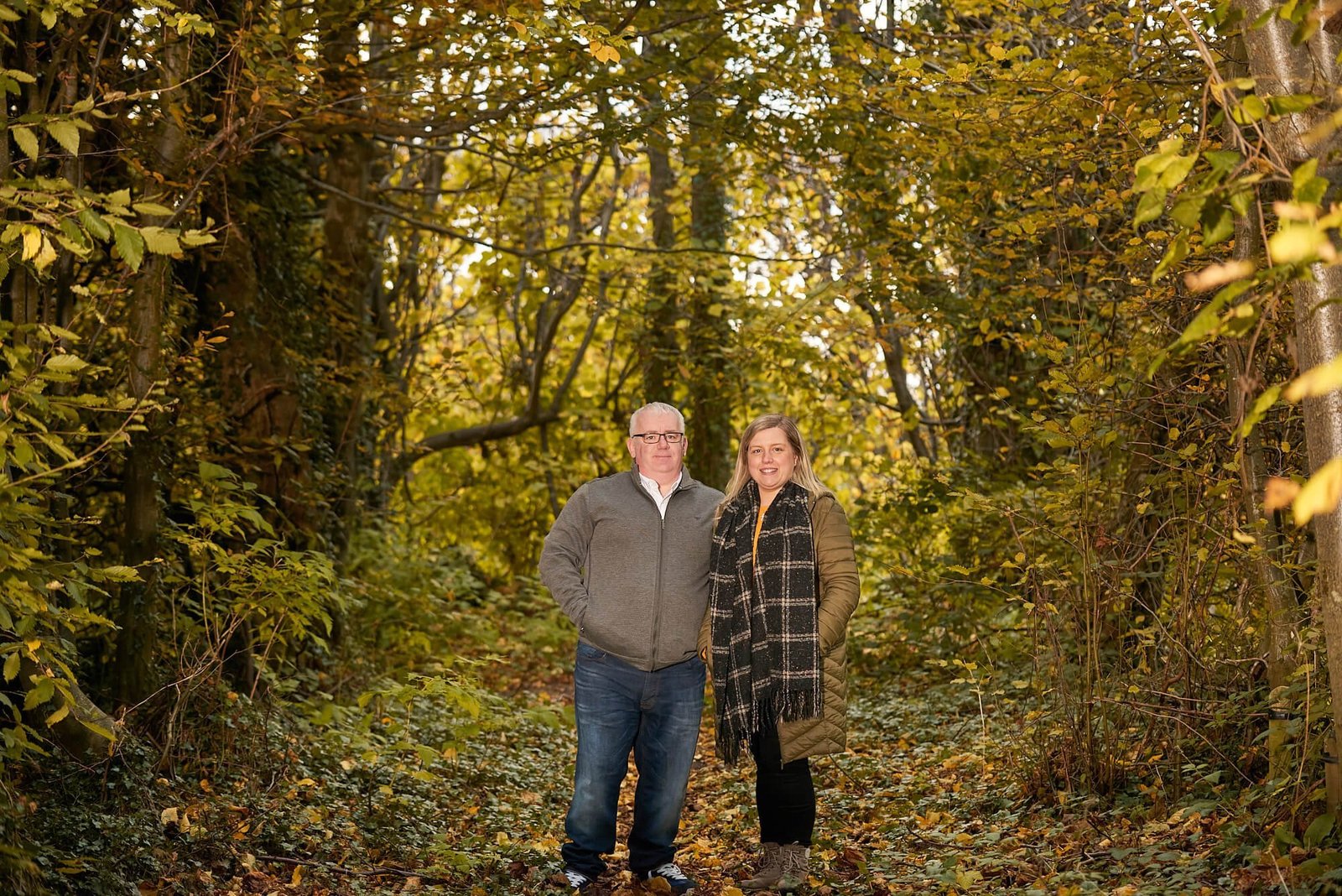 A couple standing in a wooded area during their engagement session.