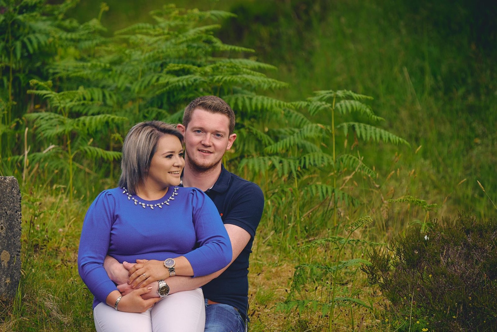 Family Photographer A couple sitting closely together in a grassy field with ferns in the background.