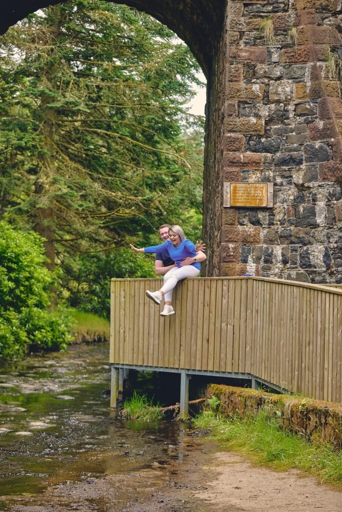 A man is standing on a wooden bridge over a stream.