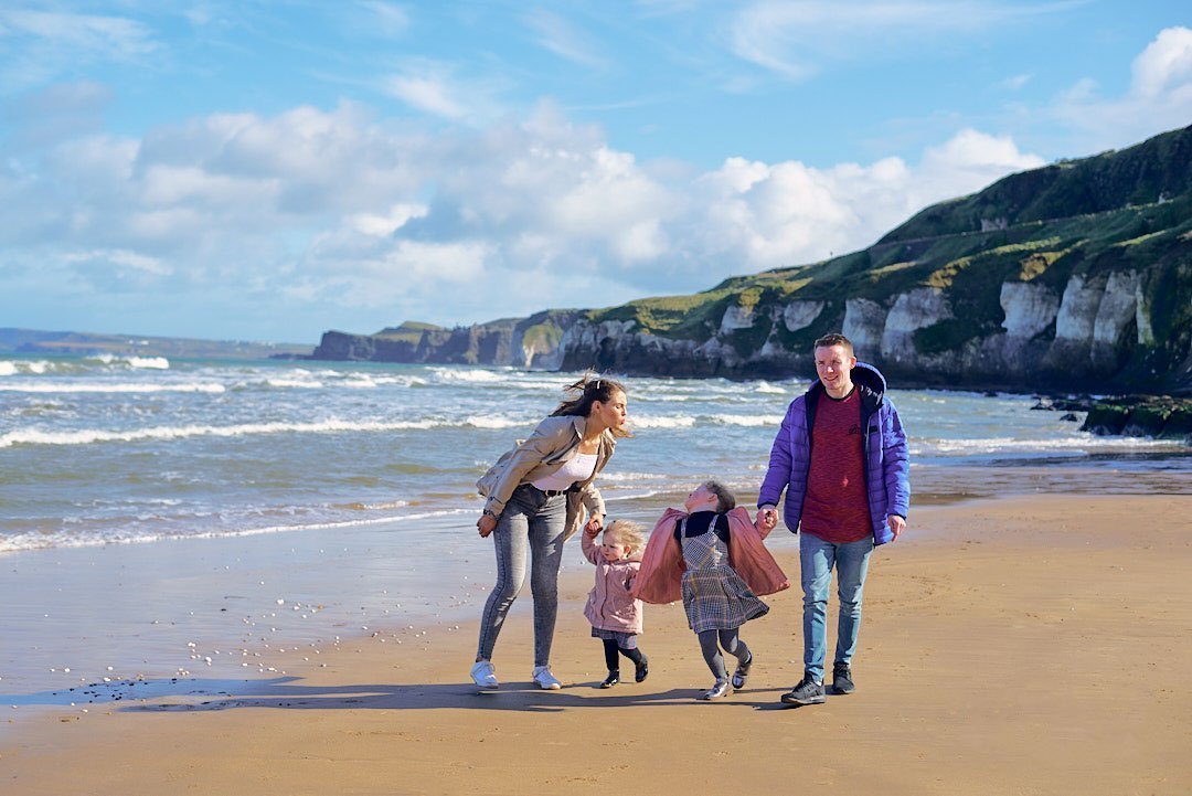 A family photographer captures moments of a family walking on a beach near the ocean.