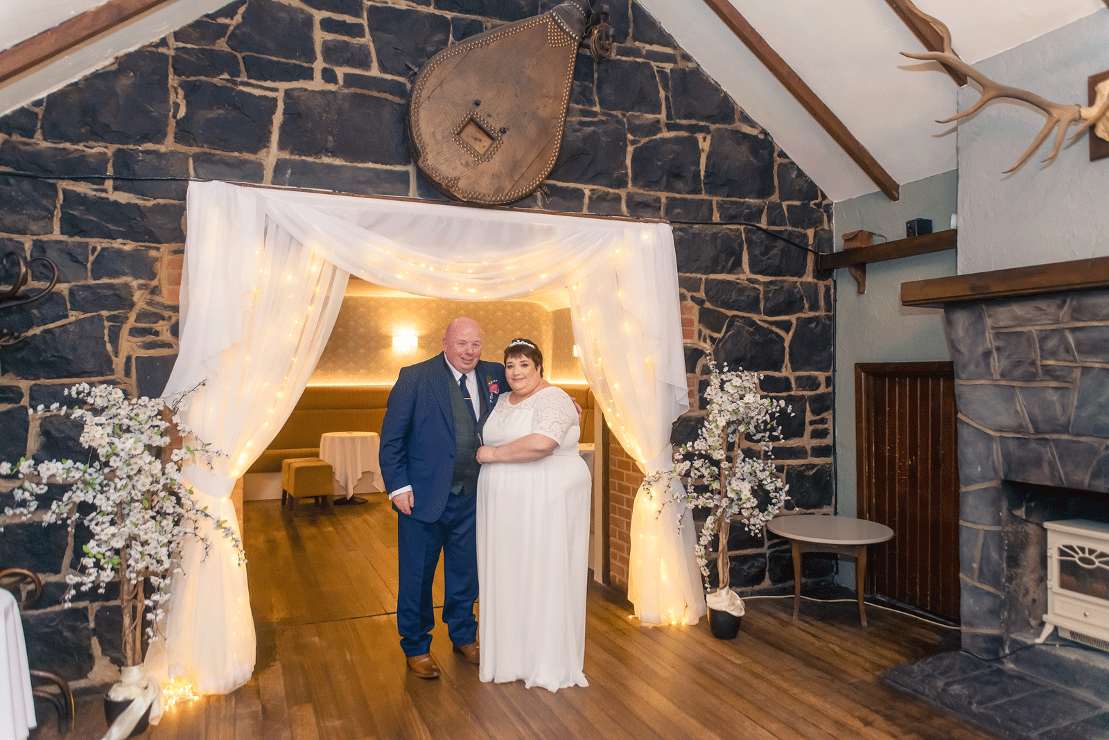 A bride and groom posing for family photographer in front of a stone fireplace.