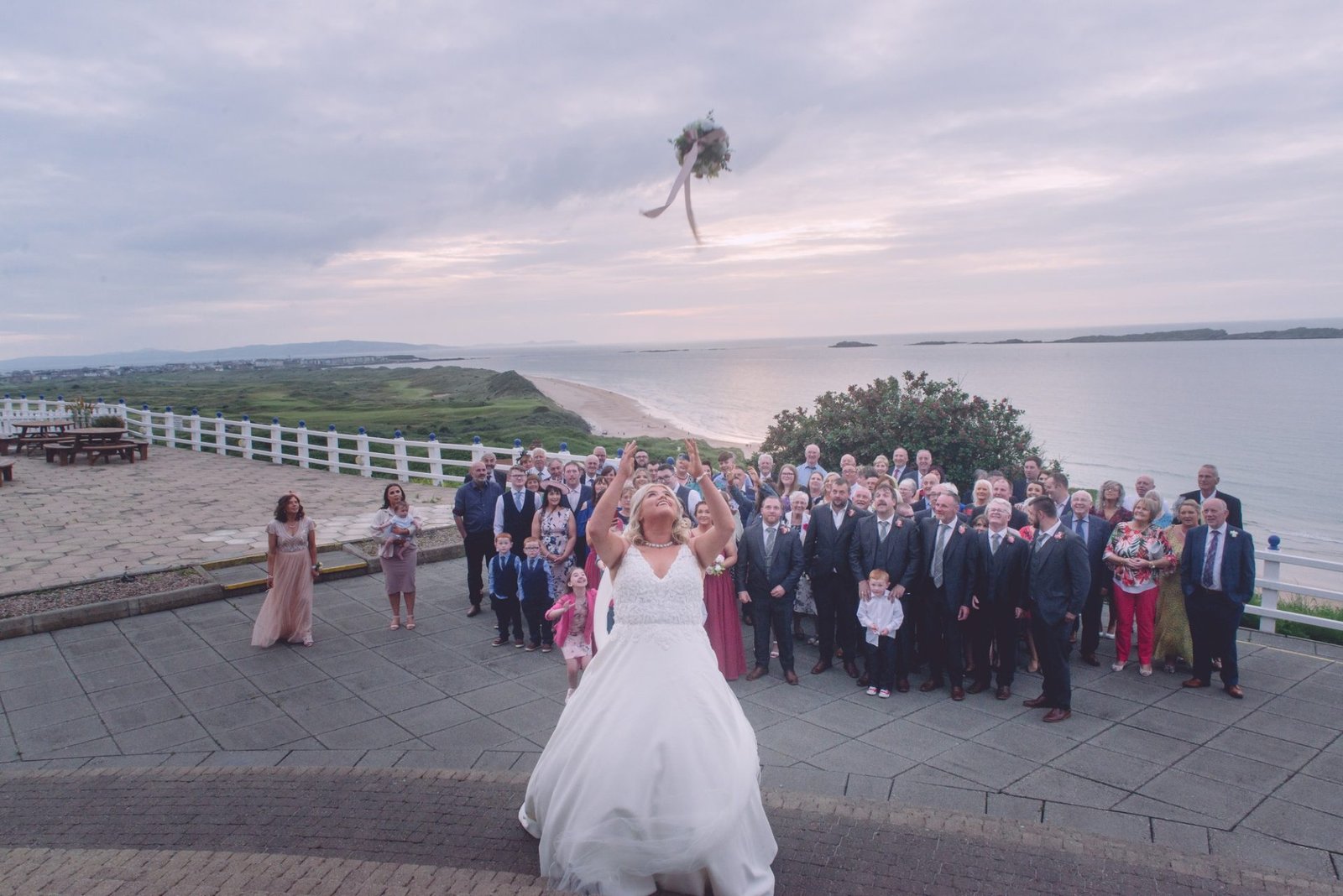 Family Photographer Bride throwing bouquet to guests at a beachside wedding celebration captured by a Portrush wedding photographer.