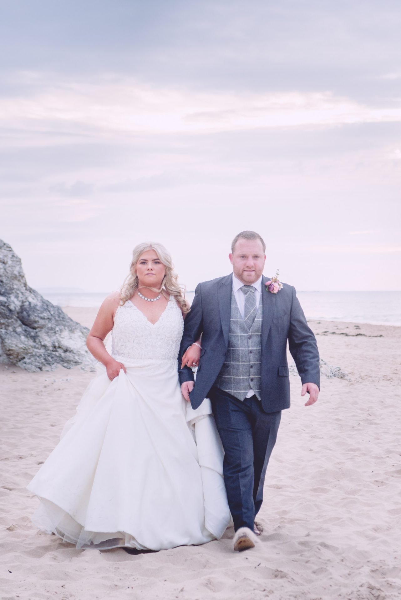 A family photographer captures the serene moments of a bride and groom walking on the beach.