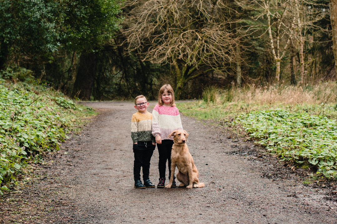 Family Photographer northern ireland Two girls and a dog standing on a path in the woods.