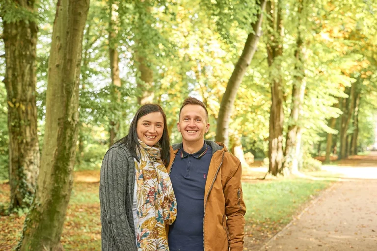 Family Photographer Two people smiling in a tree-lined pathway during autumn.