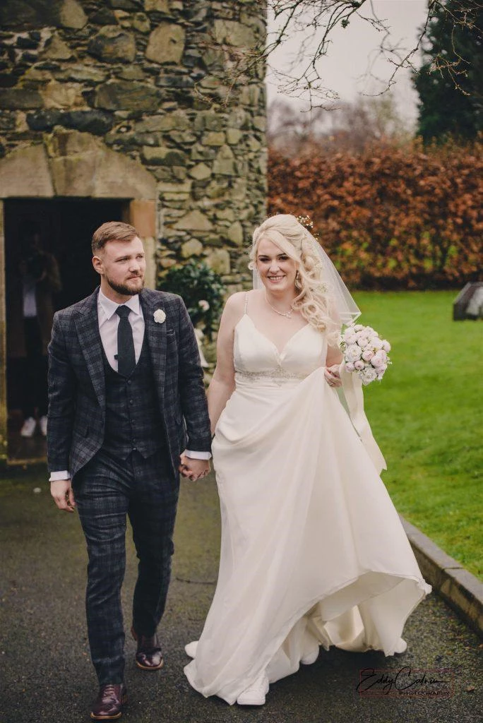 Family Photographer A bride and groom walking in front of a stone building.
