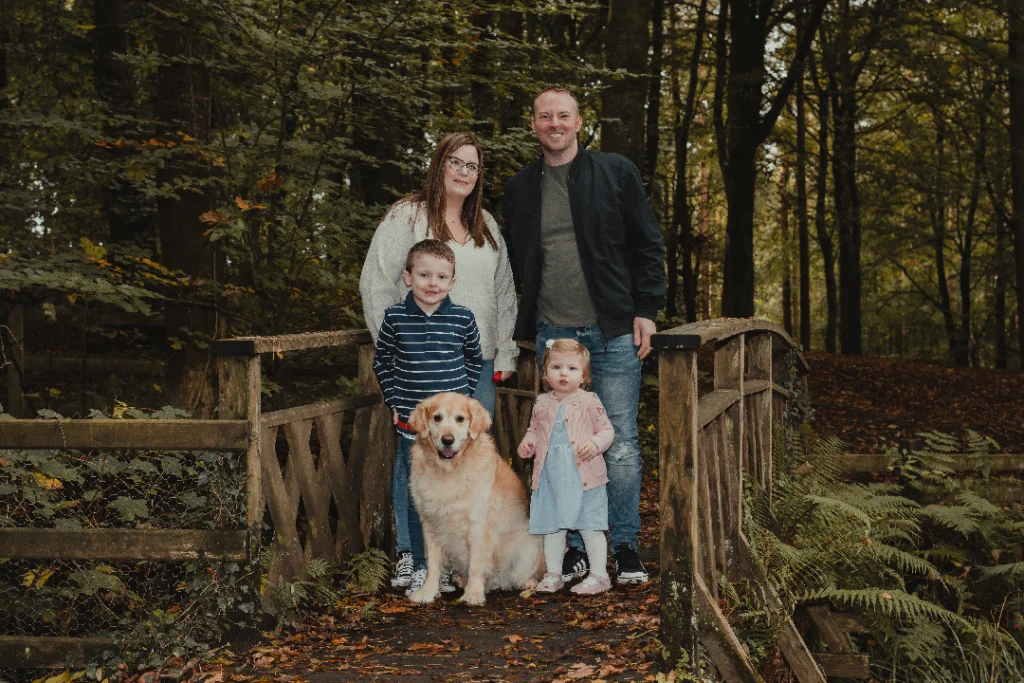 F.A.Q. 1 Family Photographer A family posing on a bridge in the woods with their dog.