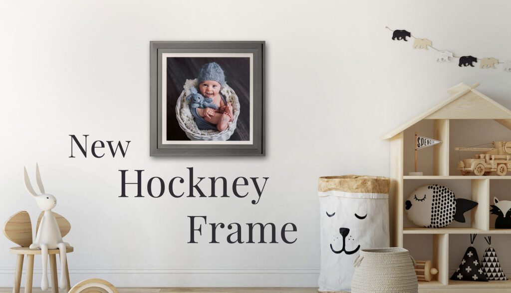 Family Photographer A baby photo in a dark frame is displayed on a light-colored wall in a child's nursery, with decorative toys and items around the room, and text on the wall that reads "new hock.