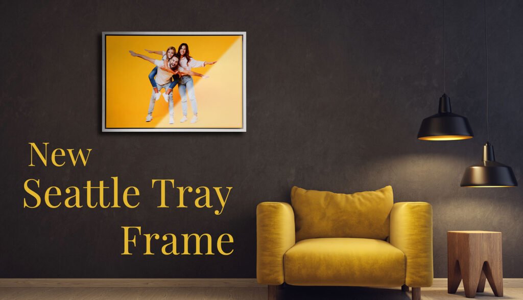 Family Photographer A stylish mustard yellow armchair and a small wooden stool sit against a dark gray wall, beneath a framed image of two people posing happily, with the caption "new seattle tray frame". a pendant lamp.